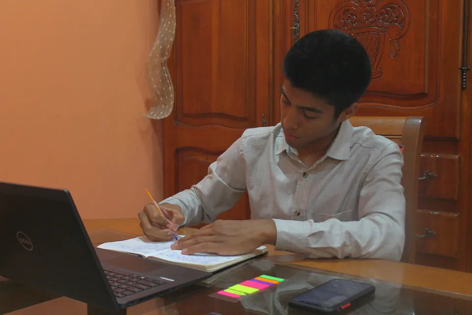 Joaquín Caballero writing in his notebook next to the laptop